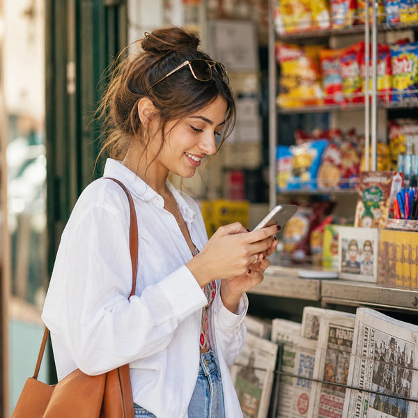 Young woman smiling at her phone at a street kiosk